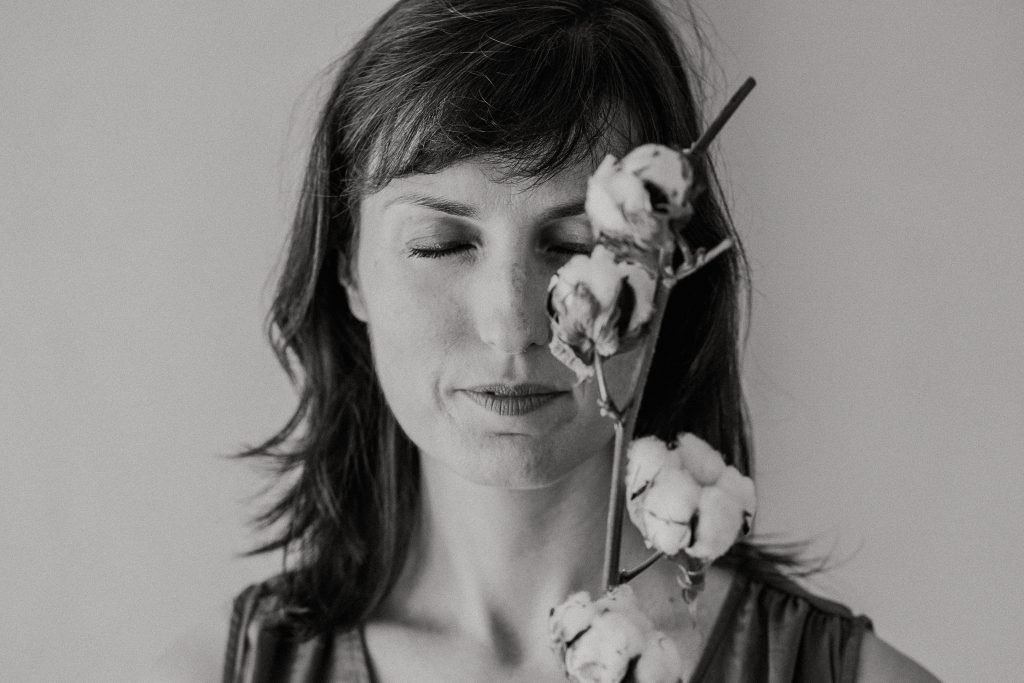 Un primo piano in bianco e nero, con gli occhi chiusi e un ramo di fiori di cotone che coprono parzialmente il volto per comunicare calma e introspezione.